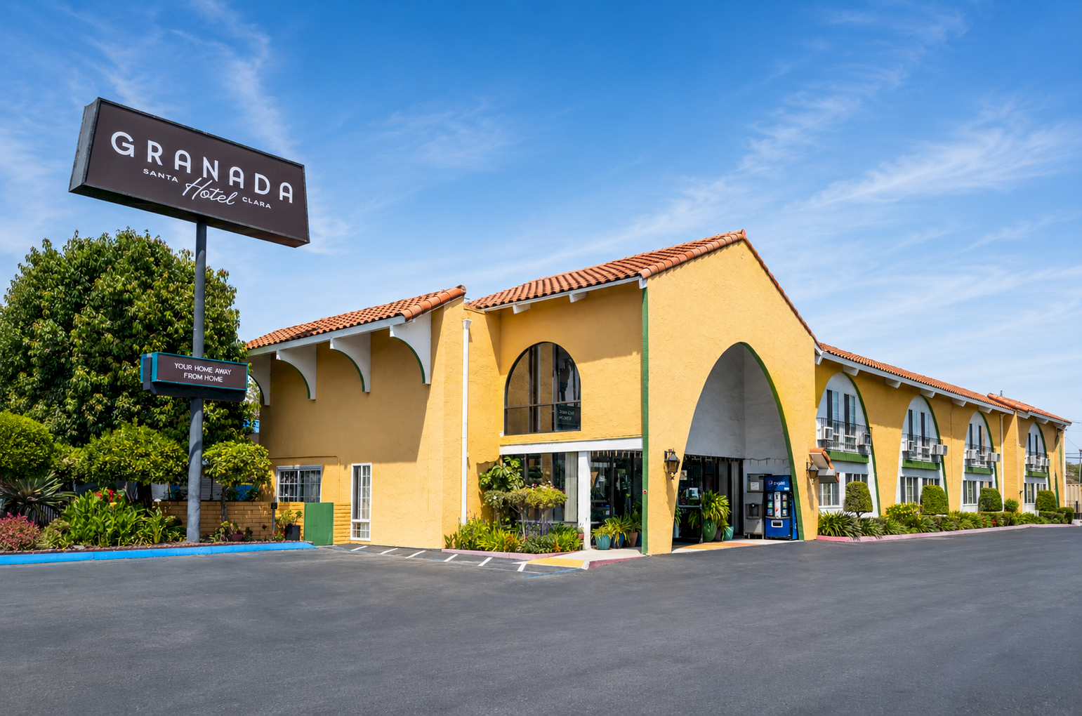 A single-story tan building with arched windows and a red-tiled roof sits under a blue sky, labeled &ldquo;Granada&rdquo; on a large sign, surrounded by a paved lot.