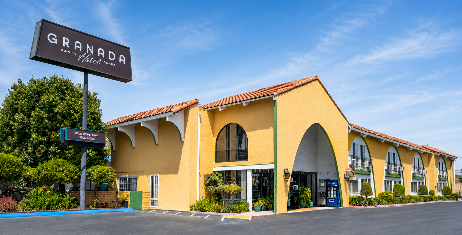 A single-story tan building with arched windows and a red-tiled roof sits under a blue sky, labeled &ldquo;Granada&rdquo; on a large sign, surrounded by a paved lot.