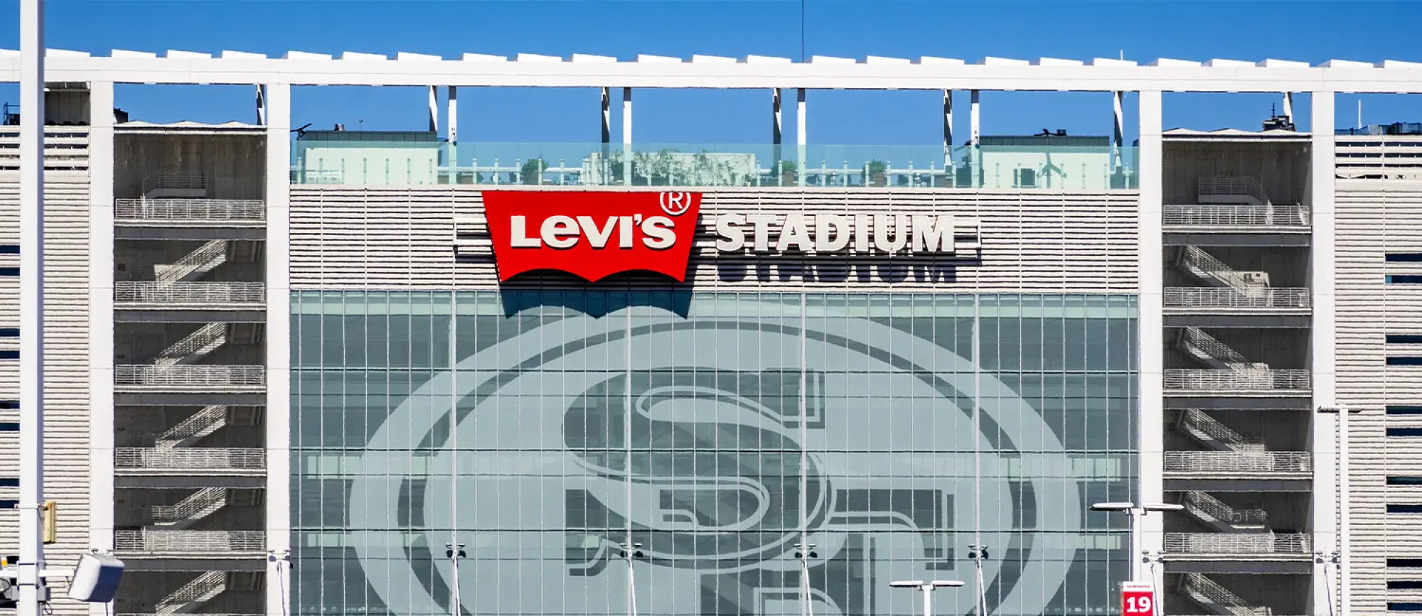 A modern stadium with Levi&rsquo;s branding on the fa&ccedil;ade, glass entry, and large San Francisco 49ers logo pattern displayed on the front.