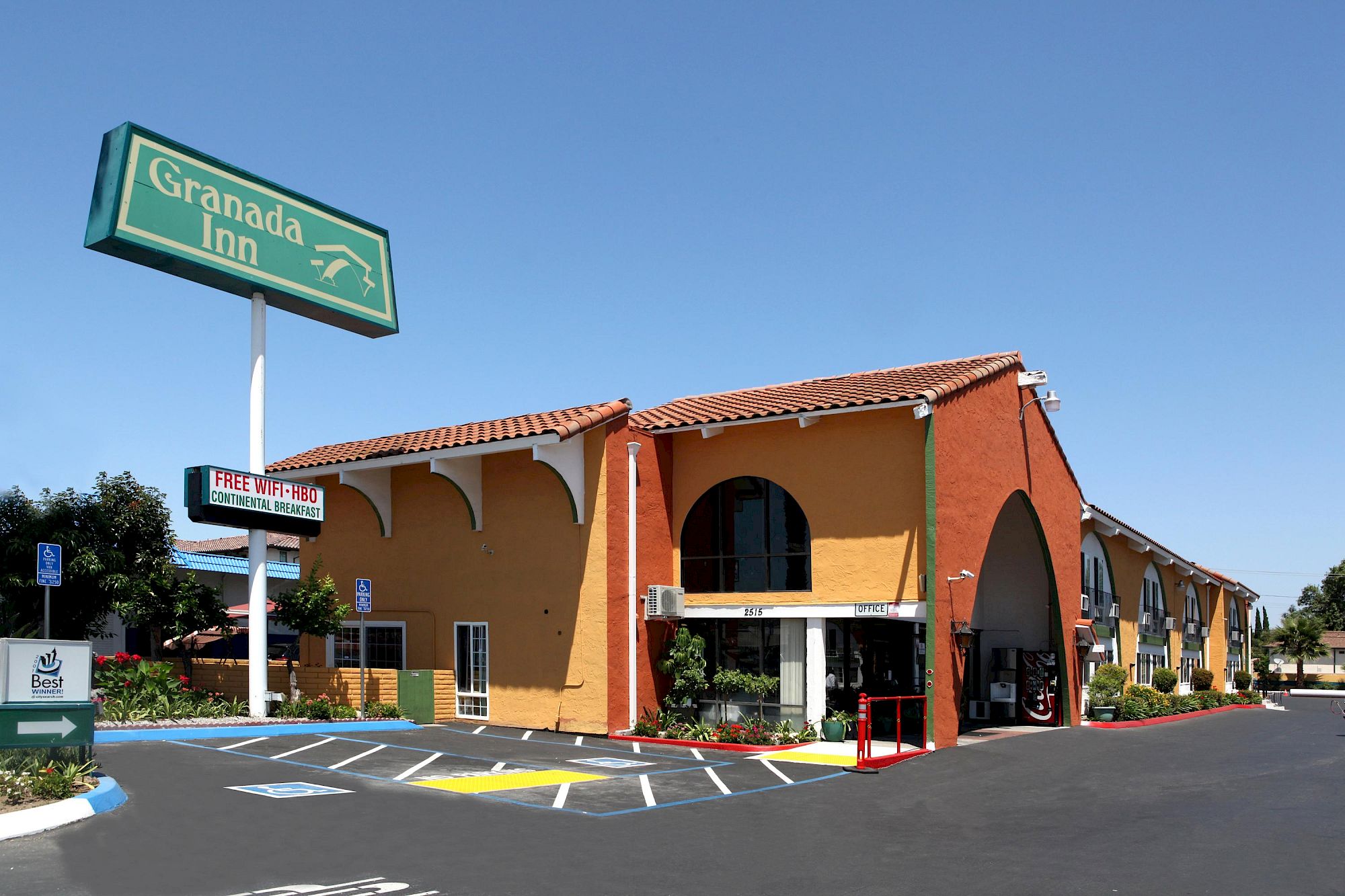 Colorful building with a curved orange facade, a green Granada Inn sign, and blue sky; parking lot and small trees nearby.