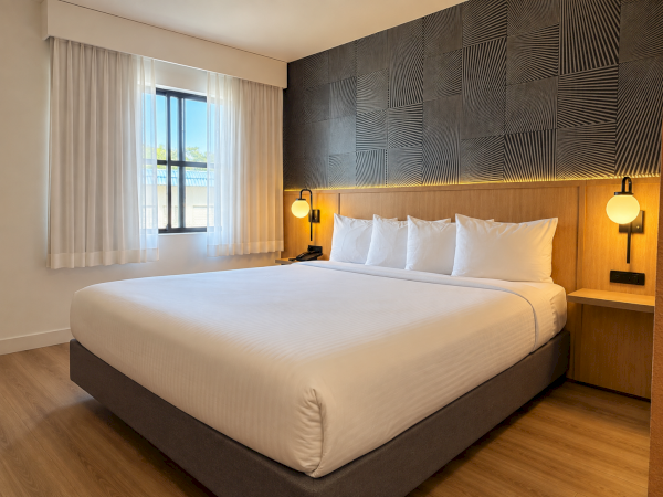 Modern hotel bedroom with a large bed, white pillows, bedside lamps, wood paneling, and geometric wall art.