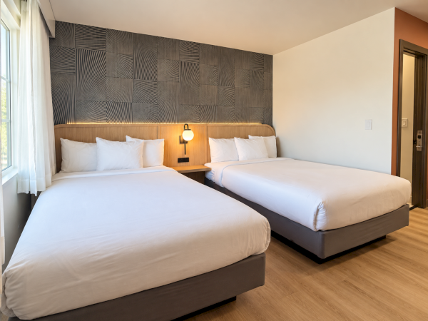 A modern hotel room with two neatly made twin beds, patterned headboard wall, and warm bedside lighting.