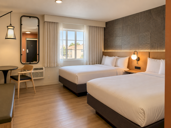 A modern hotel room with two twin beds, white linens, warm wall lights, and a window with curtains.