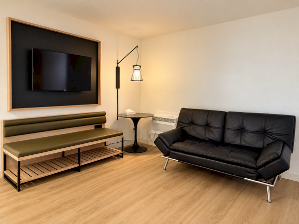 A modern living room with a wall-mounted TV, black leather sofa, round side table, and floor lamp.