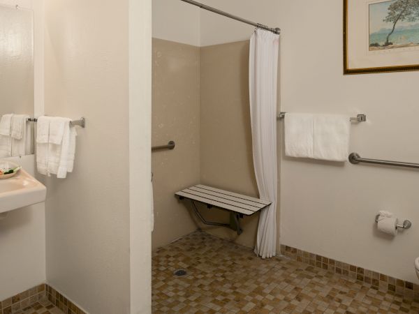 A compact bathroom with a shower stall, bench, beige tile, white towels, and a wall-mounted toilet, all in a clean, simple layout, ending with a period.