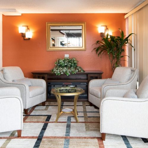 A bright, cozy living room with two white sofas facing a dark coffee table and a wall-mounted TV, warm lighting, and a plant in the corner.