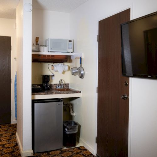 A small kitchen nook with a white refrigerator, wooden shelves, and a dark cabinet against a white wall.