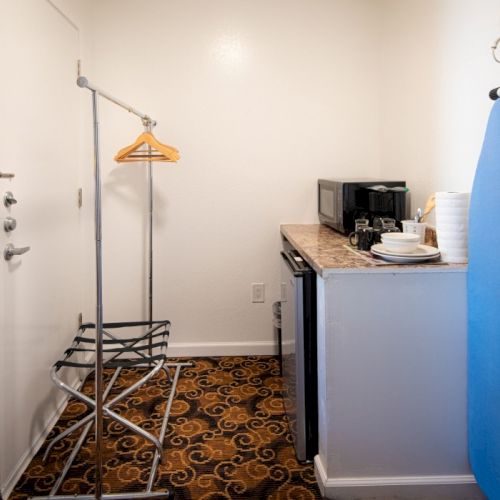 A small, cozy entry or hallway with a checkered brown floor, white walls, a blue door on the right, and a wooden shelf/valet area with a few hooks and decor.