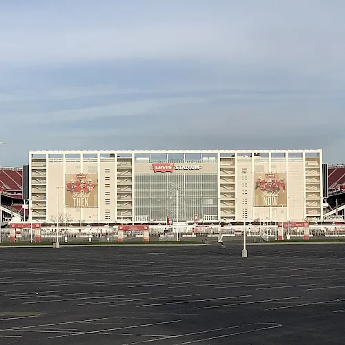 Levi’s Stadium—an empty football stadium with red seats and giant end-zone billboards under a cloudy sky.